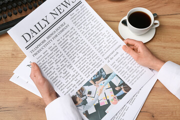 Fototapeta premium Female hand holding newspaper and cup of coffee on wooden background