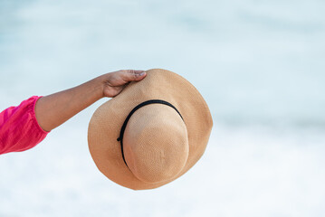 Hand holding straw hat against ocean background