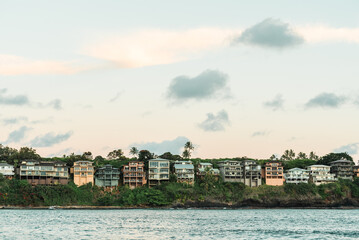Fototapeta premium Coastal homes built along green tropical hillside overlooking ocean