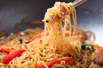 Japchae, Korean stir fried glass noodles with vegetables, pork, soy sauce and sesame oil in cooking pan and chopsticks