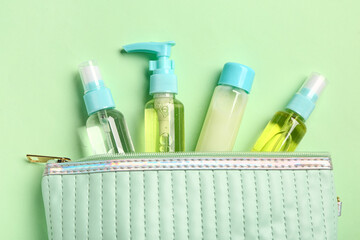 Bag with set of travel cosmetic products on green background