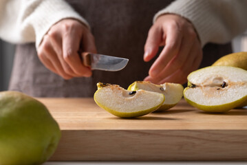 Hand holding kitchen knife and cutting pear on wooden board