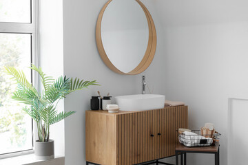 Sink bowl and bath accessories on wooden cabinet in interior of light bathroom