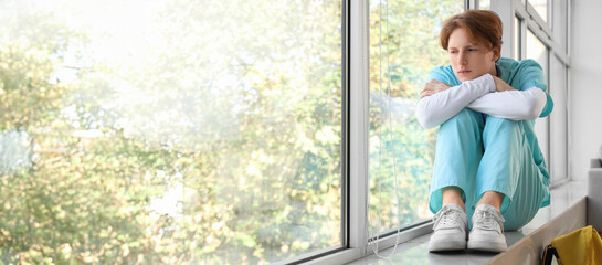 Upset male medical intern sitting on windowsill in clinic