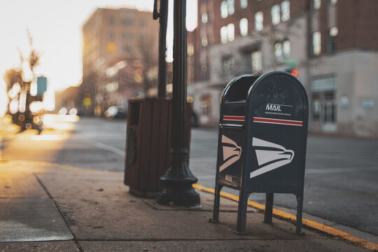 An iconic blue United States Postal Service (USPS) collection box on a city street with buildings in the background (Jefferson City, MO - Dec. 24, 2025). For Editorial Use Only.