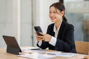 Asian businesswoman holding phone work on laptop computer  at the office with calculator document doing planning analyzing the financial report, business plan investment, finance analysis concept.
