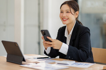 Asian businesswoman holding phone work on laptop computer  at the office with calculator document doing planning analyzing the financial report, business plan investment, finance analysis concept.
