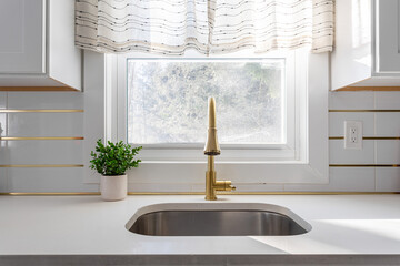 Modern kitchen sink with brass faucet, white countertop and window in bright minimalist interior