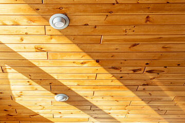 Warm wooden ceiling with natural sunlight and geometric shadows creating abstract interior texture