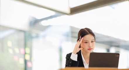 Fototapeta premium Portrait of a confident and smiling Asian business woman working on tablet at her desk in a modern office. 