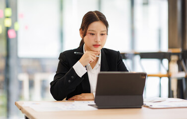 Fototapeta premium Portrait of a confident and smiling Asian business woman working on tablet at her desk in a modern office. 