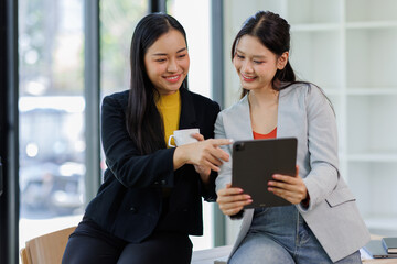Obraz premium Two young lady colleagues discussing new project, businesswomen using digital tablet together in office