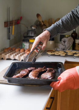 Hombre usando guante de silicona pone sobre la mesa fuente con carne cocida