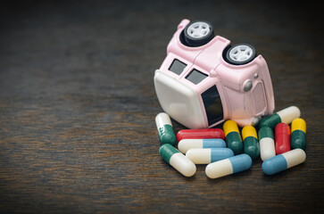 Medicated Driving Concept: Pink Toy Car Flipped Over on a Pile of Colorful Medicine and Drugs