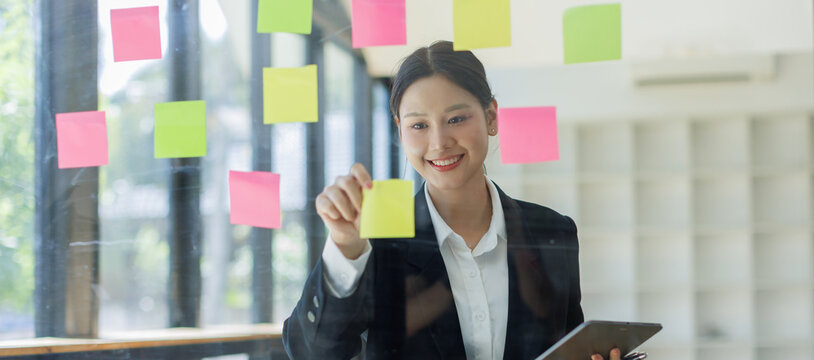 Business asian woman use post it notes to share idea sticky note on glass wall, planning and Brainstorming thinking sticky History notes concept.
- Powered by Adobe