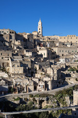Obraz premium historic sassi di matera cityscape in basalicata, italy, featuring ancient stone houses and the cathedral bell tower under a clear blue sky at sunny daylight.