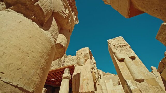 Low angle view of colossal ancient statue and massive stone columns at the Temple of Hatshepsut in Luxor, Egypt, highlighting monumental ancient Egyptian architecture