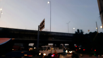 Blurred urban scene at dusk with an elevated road and streetlights, showing vehicle lights on the street below.