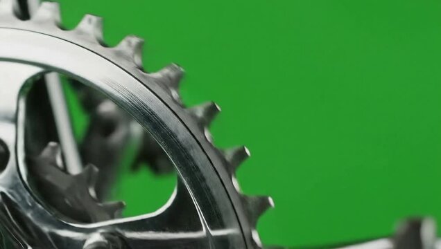 Close-up of a bicycle chainring rotating against a green screen.