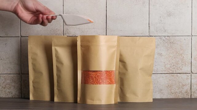 Woman pouring lentils into stand-up pouch at wooden table, closeup