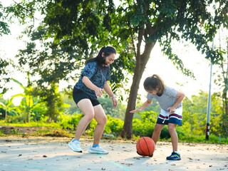 Mother and daughter played basketball together on an outdoor court during sunset.