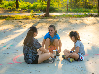 Asian mother and daughters sitting on court, resting and talking after playing basketball.
