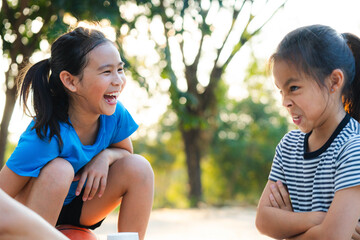 Two happy Asian sisters laughing and making funny faces while playing outdoors.