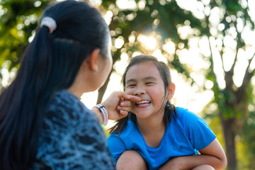 Affectionate Asian mother playing and pinching her daughter's cheek with love.