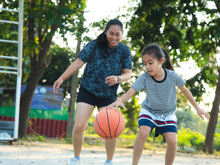 Mother and daughter played basketball together on an outdoor court during sunset.