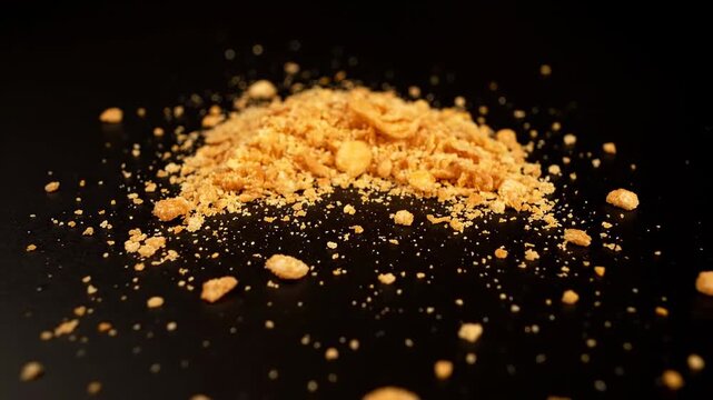 Close-up of a golden pile of crushed crackers and scattered crumbs on a glossy black surface closeup