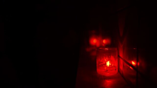 Red candle in a glass jar casting a warm glow, reflected in a nearby surface. Dark club atmosphere