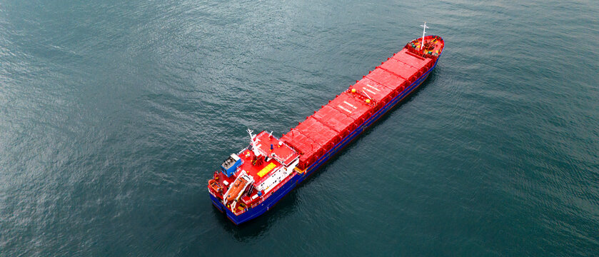 Aerial shot of a long red bulk carrier ship empty of cargo sailing on the open sea showcasing the vast red deck and storage hatches used for international trade transport