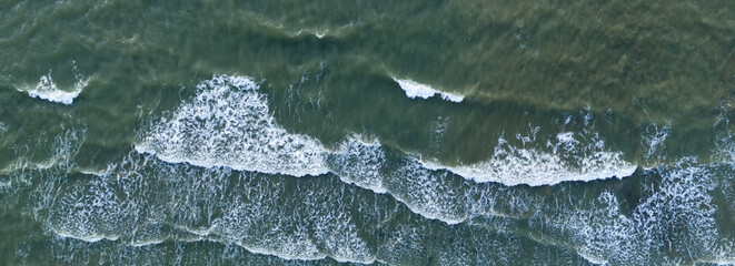 Aerial top down shot of white foamy waves crashing on the surface of dark green sea water creating natural abstract patterns and textures of the moving ocean power