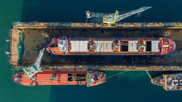 Overhead drone view of a cargo ship in a floating dry dock with its hatches open for inspection surrounded by the turquoise sea water of the shipyard harbor