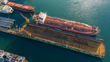 Detailed aerial shot of a rusty red ship hull in a dry dock being prepared for sandblasting and painting as part of the heavy maintenance process in a shipyard © Buğra Kaan Ersoy
