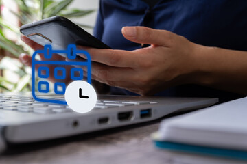 A person uses their smartphone in front of a computer with a calendar and clock icon. Concept of organizing or scheduling an event.