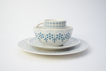 Set of elegant white ceramic tableware with blue floral patterns, including plates, bowl, and cup, isolated on white background