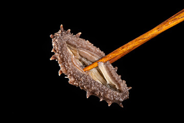 Raw sea cucumber trepang with chopsticks on black background