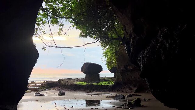 Beautiful sunset near a natural cave on Soan Galuh Beach in Tabanan. A beach with black volcanic sand and bizarre mushroom-shaped rocks on the island of Bali, Indonesia. 4К