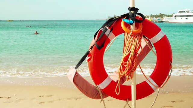 A lifebuoy overlooking a sandy beach where people relax and swim. Life-saving equipment for saving people on the water.