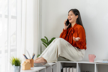 Connected & Creative: A vibrant young woman radiates positivity as she works from a cozy home office, effortlessly multi-tasking and engaging in a cheerful phone call. 