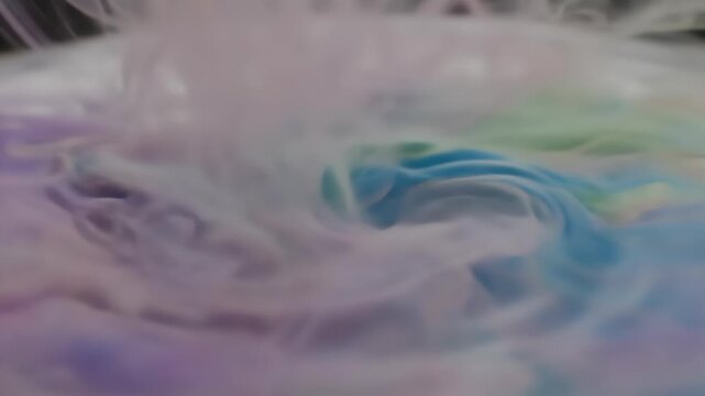 A clear optical lens is carefully positioned while colorful ink droplets diffuse and swirl in clear liquid. Subtle reflections and soft lighting create an ethereal atmosphere.