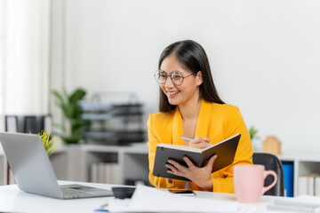 Focused Businesswoman at Work: A businesswoman, radiating positivity and purpose, sits attentively at her desk, engrossed in her work, a laptop and notebook aiding her.