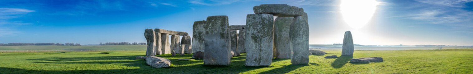 Visitors explore Stonehenge in the early morning light surrounded by green grass and clear skies