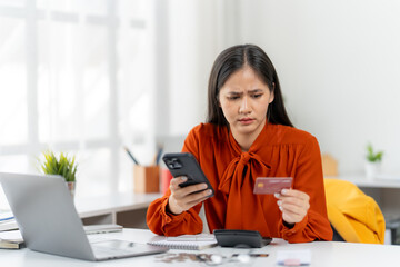 Financial Concern: A woman's face, etched with worry, holds a credit card in one hand while intently reviewing financial details on her phone.