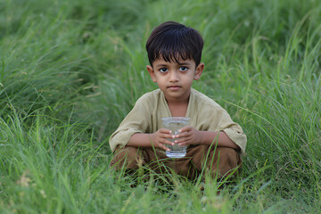 a young boy sitting in the grass holding a glass of water
