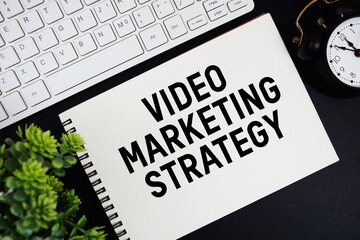 Video Marketing Strategy text written on notepad with keyboard and alarm clock on black background
