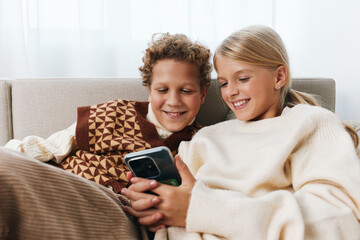 Fototapeta premium Authentic moment of playful learning and family lifestyle as two children share a cozy screen moment on the sofa, smiling together in a warm, relaxed setting.