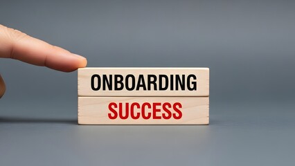 A hand points to wooden blocks spelling 'ONBOARDING SUCCESS' on a grey background, symbolizing successful integration.