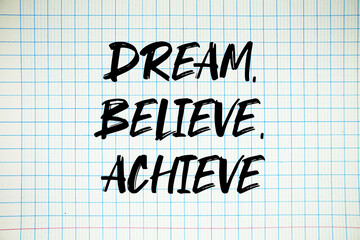 Fototapeta premium Dream, Believe, Achieve text written on white notebook sheet with grid